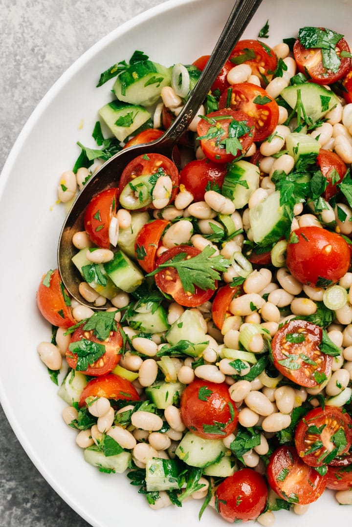 White bean and tomato salad in a white serving bowl with a vintage serving spoon.