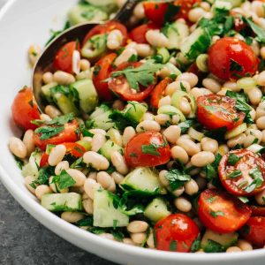 Side view, white bean salad with tomato, cucumber, and parsley in a large serving bowl.