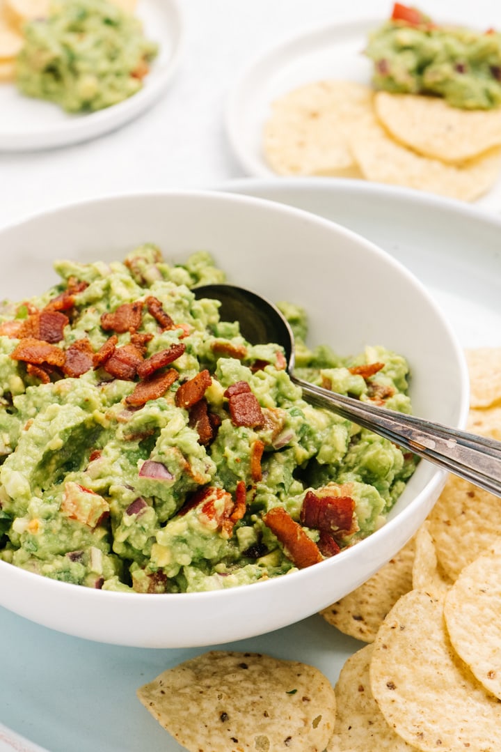 Side view, homemade guacamole with bacon in a white bowl surrounded with tortilla chips. 