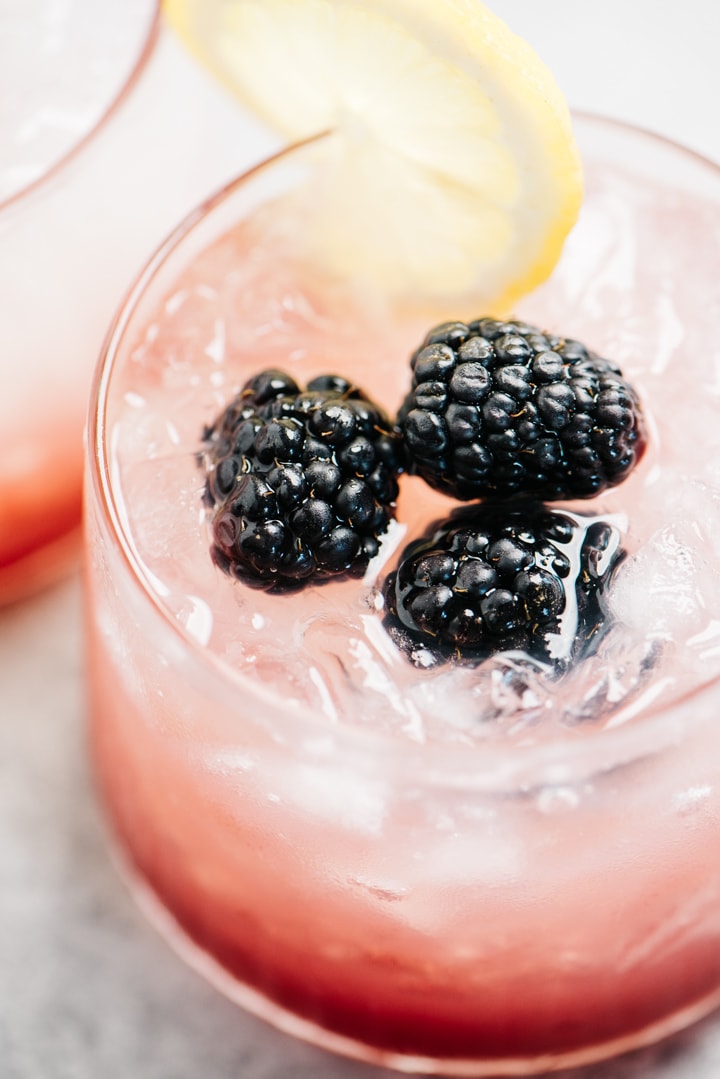 A gin and blackberry cocktail garnished with a lemon wedge and fresh blackberries.