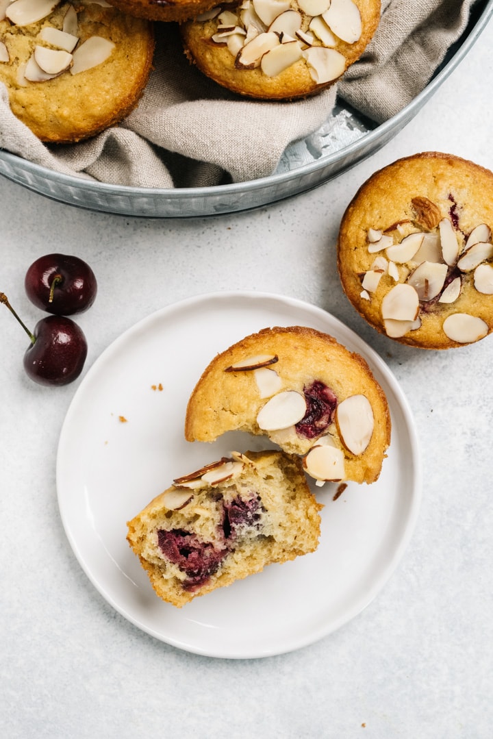 A cherry almond muffin broken in half on a white plate. 