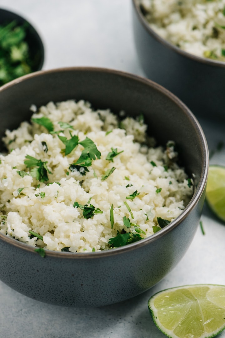 Side view, a bowl of cauliflower rice seasoned with cilantro and lime.