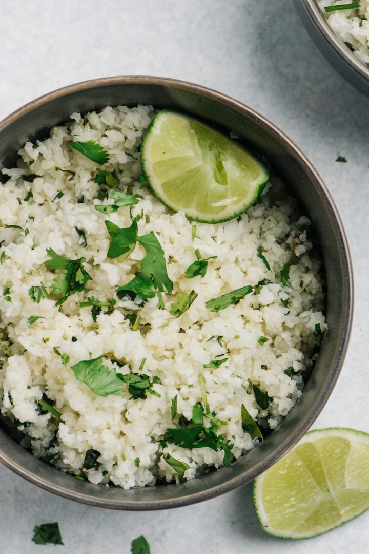 A bowl of cilantro lime cauliflower rice with lime wedges and fresh cilantro.