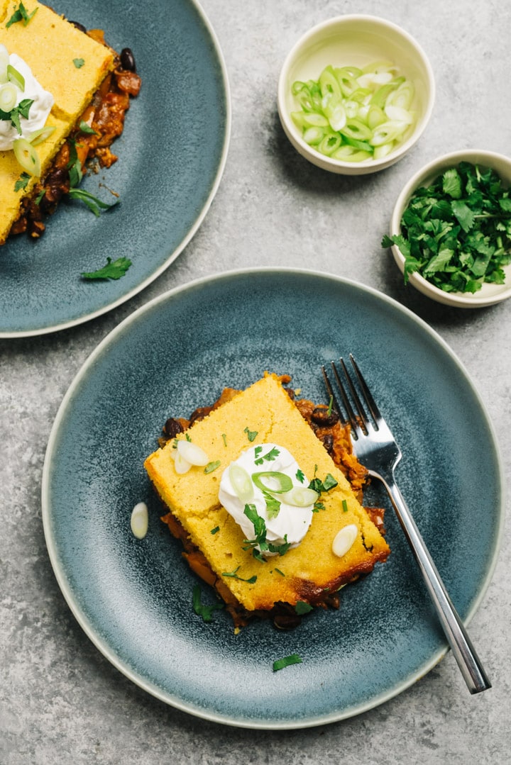 A slice of pulled pork tamale pie on a blue plate topped with sour cream, cilantro, and sliced green onions.