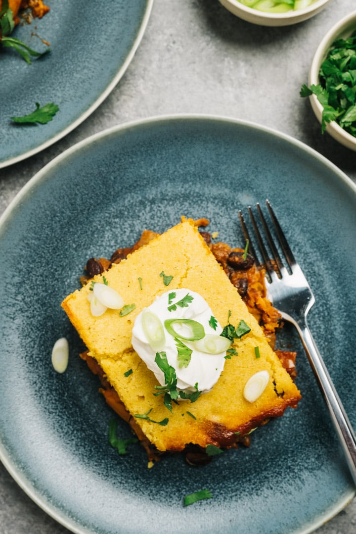 A slice of tamale pie made using leftover pulled pork on a blue plate with a silver fork.