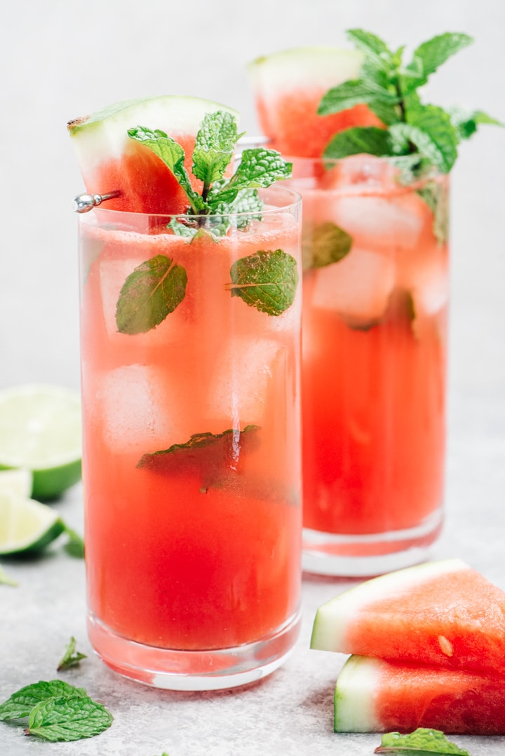 Two watermelon mojitos in tall collins glasses garnished with mint and a watermelon wedge.