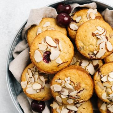 A batch of cherry muffins in a bowl lined with a tan linen napkin.
