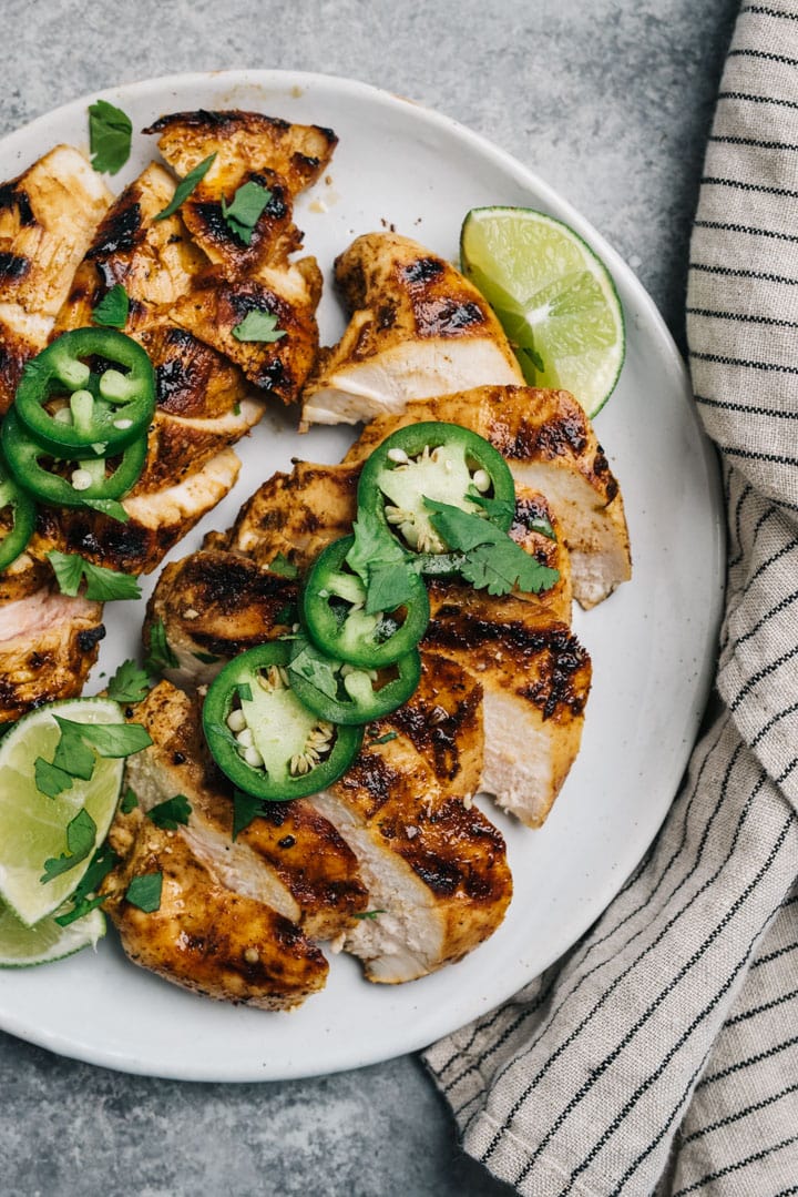 A white platter of sliced chili lime chicken breasts topped with cilantro and jalapeno.