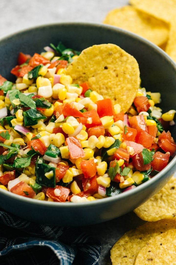 A blue bowl of roasted corn salsa surrounded with tortilla chips.