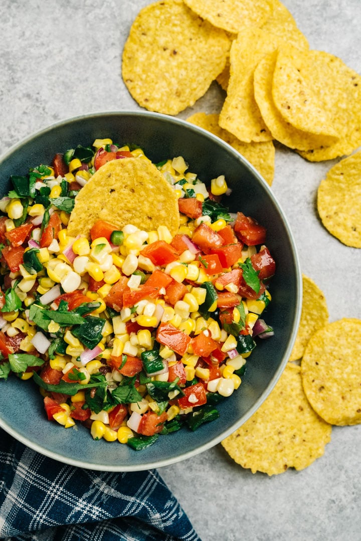 Side view, corn salsa in a blue bowl surrounded with corn tortilla chips.