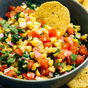 A blue bowl of roasted corn salsa surrounded with tortilla chips.