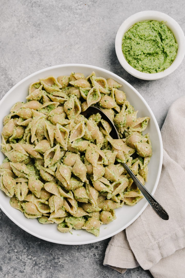Whole wheat shells tossed with pesto made with broccoli, basil, and pine nuts in a large pasta bowl with a small bowl of pesto on the side.
