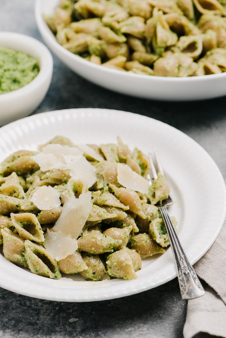 Side view, a plate of pasta tossed with broccoli pesto on a table alongside a large serving bowl and a small bowl of pesto.