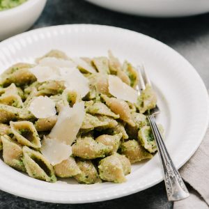 Side view, a plate of pasta tossed with broccoli pesto on a table alongside a large serving bowl and a small bowl of pesto.