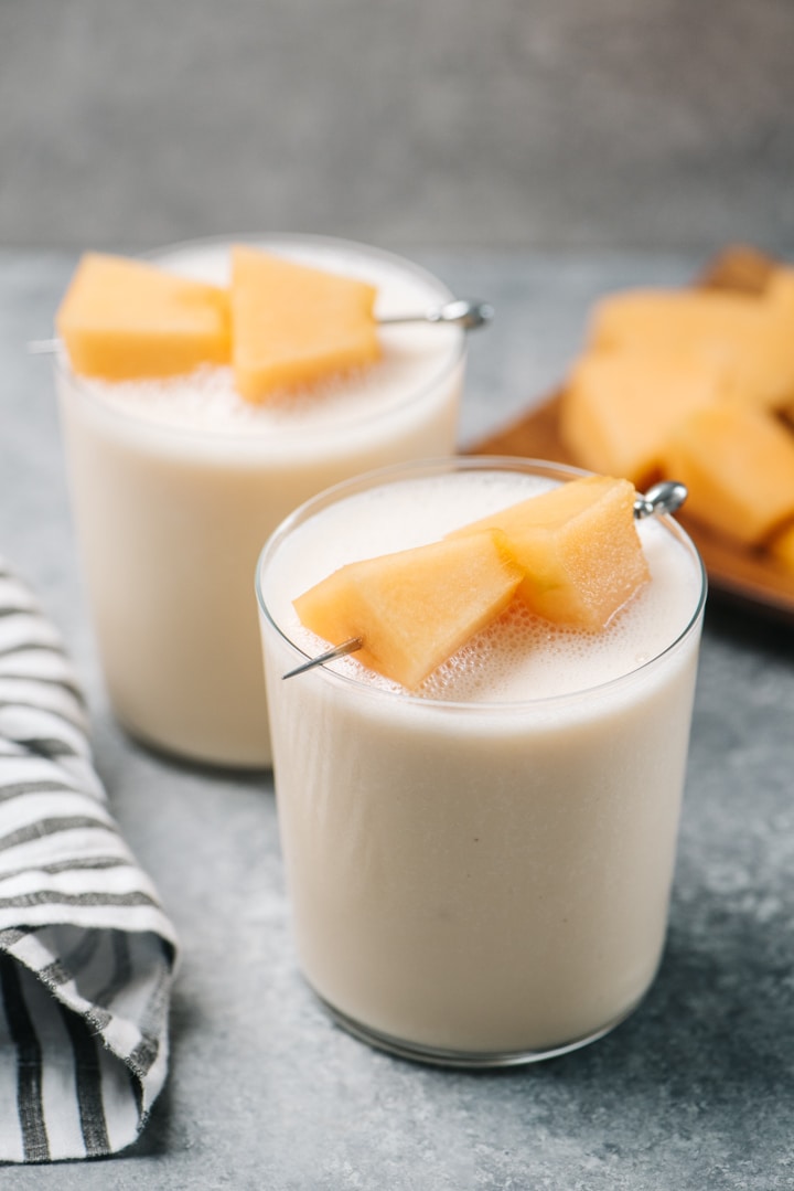 Two cantaloupe smoothies on a cement background with a striped linen napkin. 