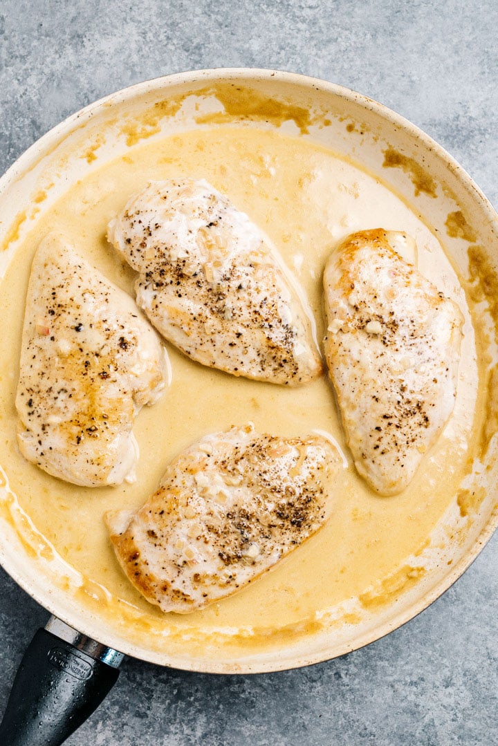 Four chicken breasts in a creamy lemon sauce in a skillet.