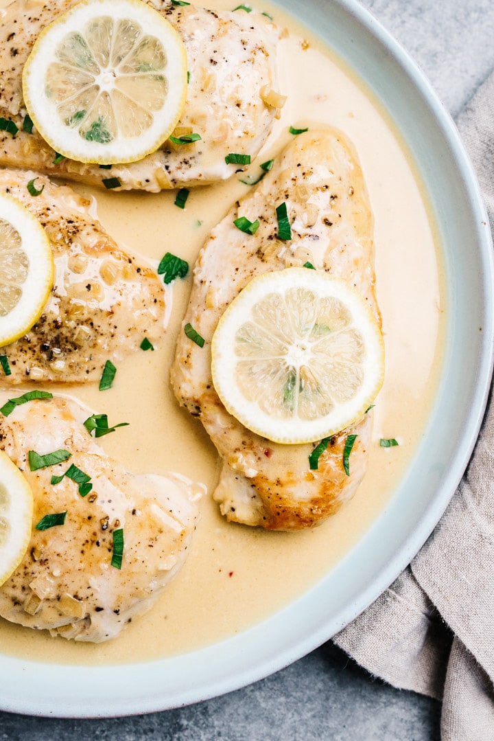 A blue serving platter filled with creamy lemon chicken, garnished with lemon slices and parsley. 