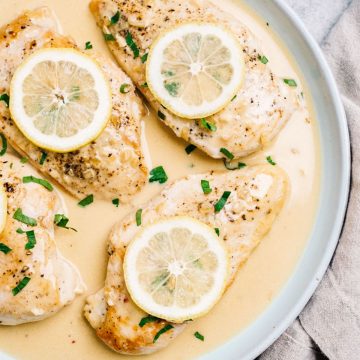 Creamy lemon chicken breasts on a blue plate garnished with lemon slices and parsley.