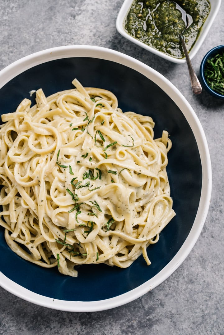 A large serving bowl of pesto cream sauce tossed with fettuccine noodles. 