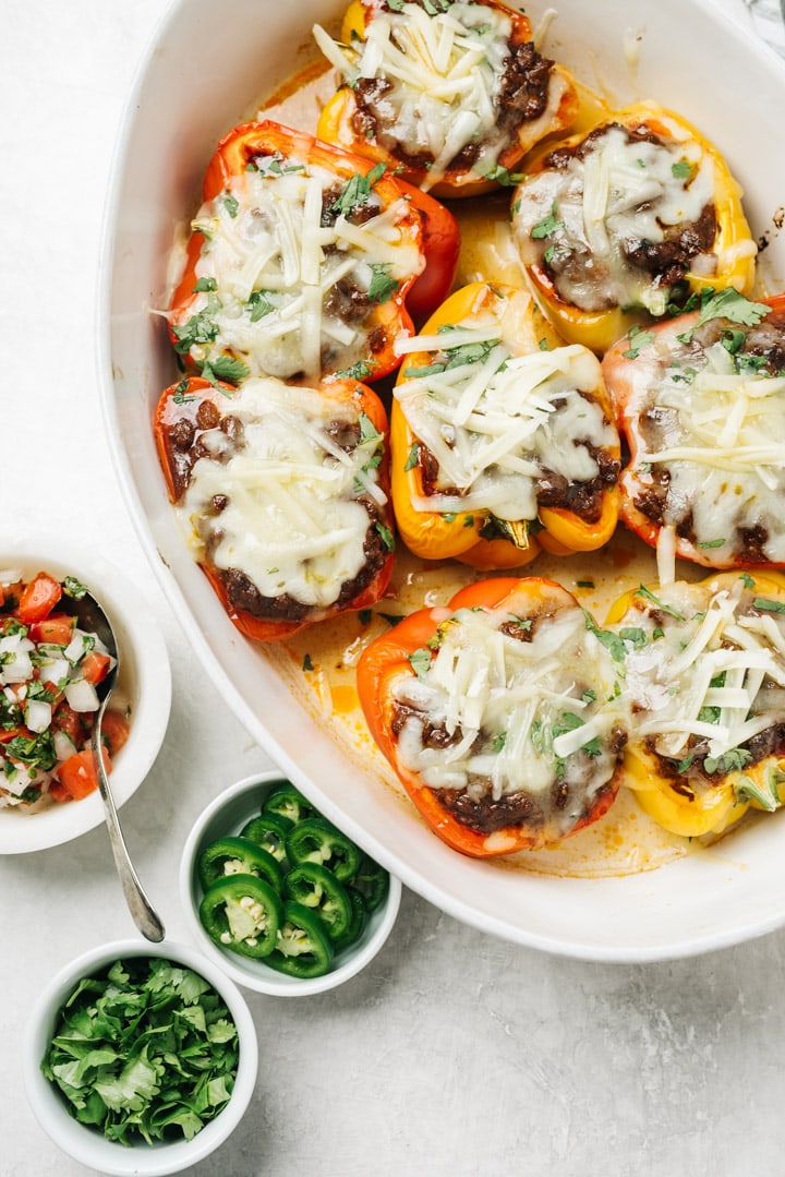 A casserole dish filled with mexican keto stuffed peppers, with small bowls of garnish on the side.