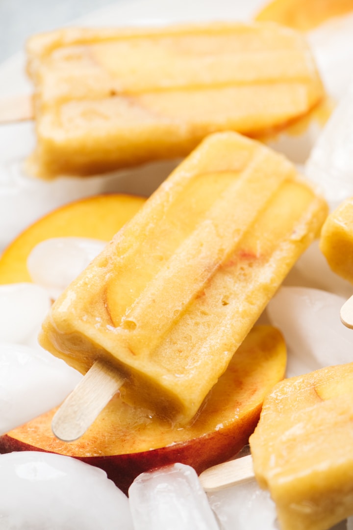 Side view, boozy white wine and fruit popsicles on a plate with ice and slices of peaches.
