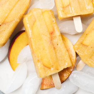Boozy popsicles on a plate with ice and slices of fresh peaches and nectarines.