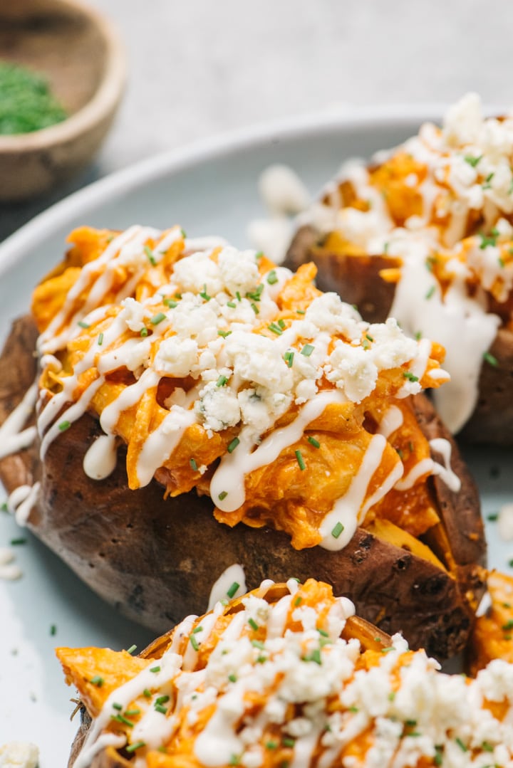 A baked sweet potato stuffed with buffalo chicken and topped with ranch and blue cheese crumbles on a blue plate.