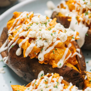 A baked sweet potato stuffed with buffalo chicken and topped with ranch and blue cheese crumbles on a blue plate.