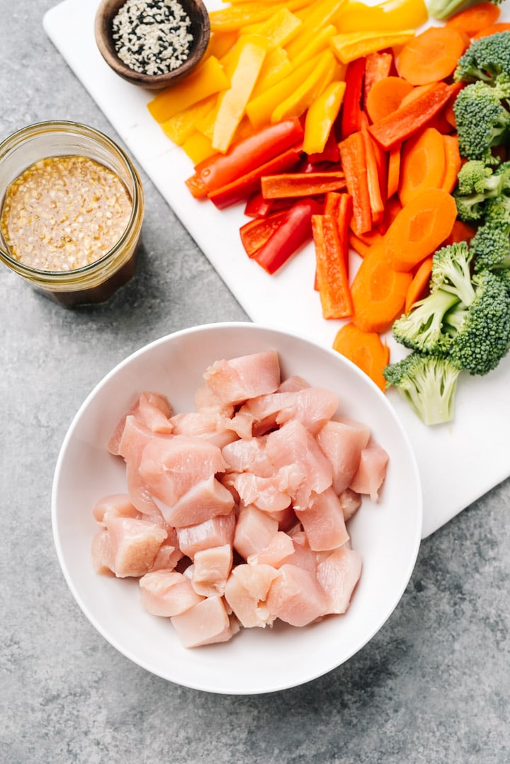 The ingredients for a healthy chicken stir fry recipe arranged on a cutting board on a cement surface.
