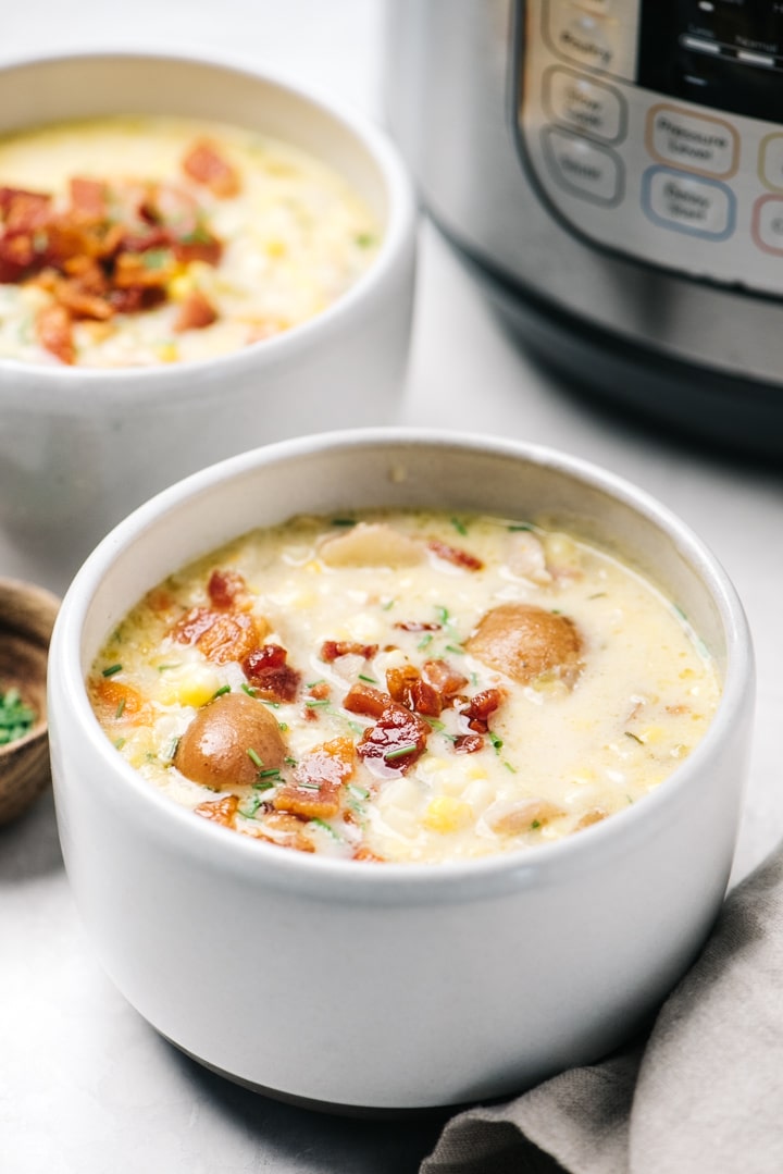 Side view, two bowls of corn chowder next to an Instant Pot on a cement background.