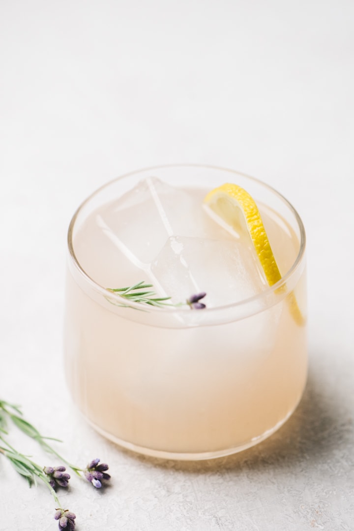 A lavender cocktail with gin, lemon juice, and lavender simple syrup on a cement background.