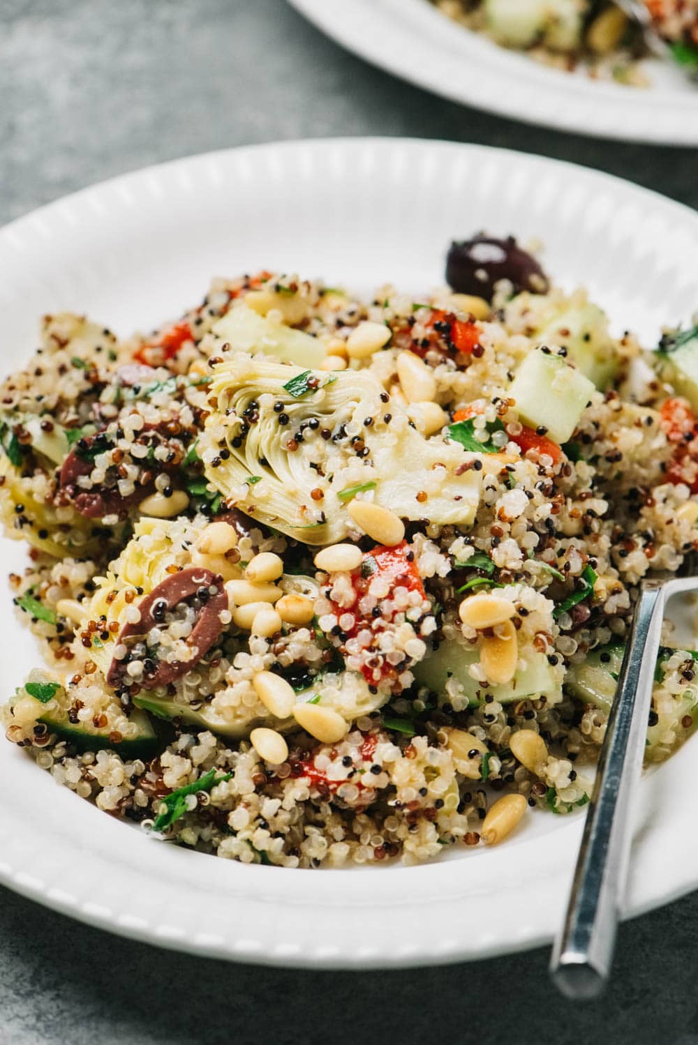 Side view, mediterranean quinoa salad on a white plate with a silver fork.