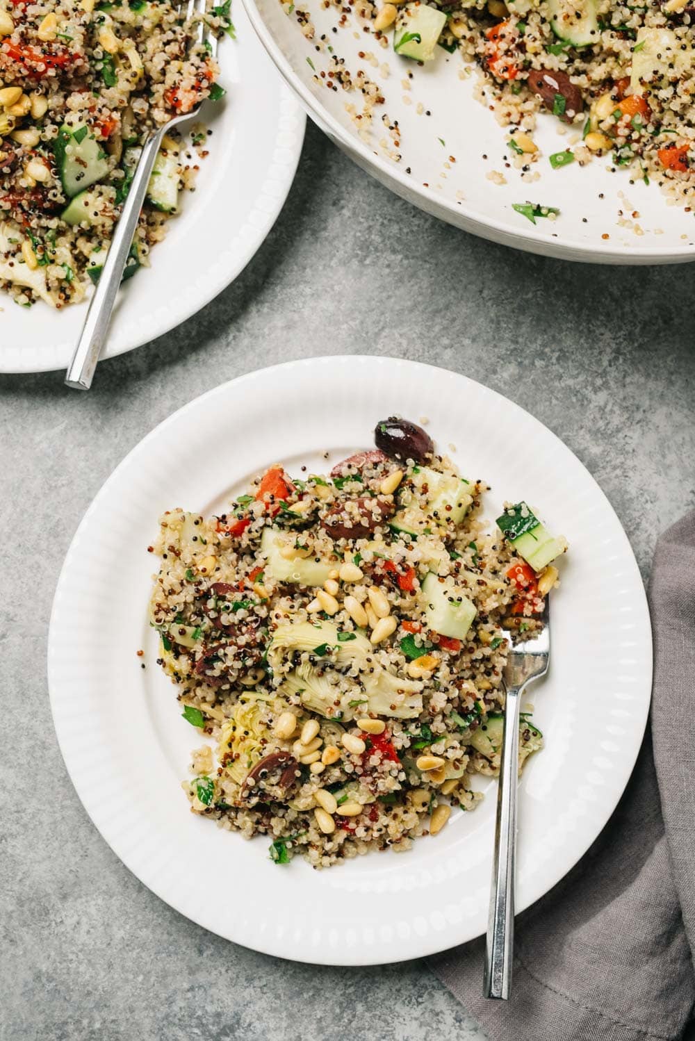 Two servings of mediterranean quinoa salad on a cement background with a grey linen napkin.