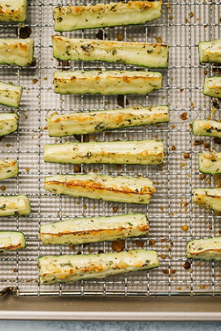 Roasted zucchini wedges with parmesan on a cool rack nested over a baking sheet.