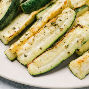 Side view, a stack of parmesan roasted zucchini wedges on a cream colored plate.
