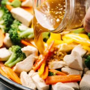 Side view, pouring stir fry sauce into a skillet with chicken and vegetables.