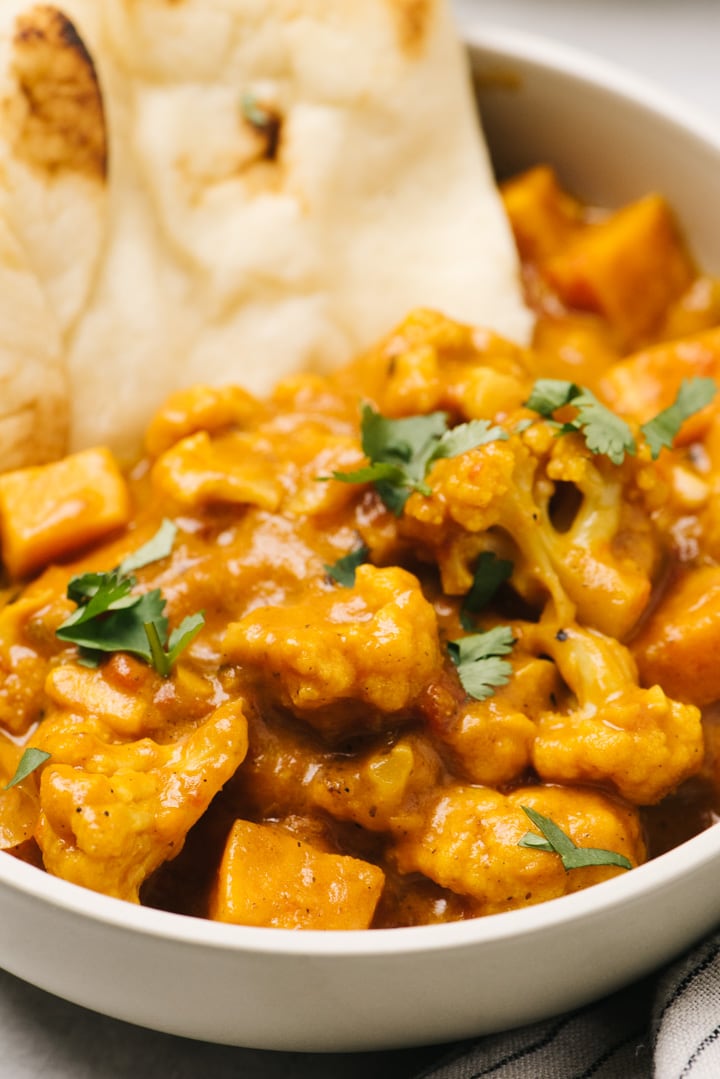 Side view, cauliflower sweet potato curry in a bowl with several slices of naan bread.