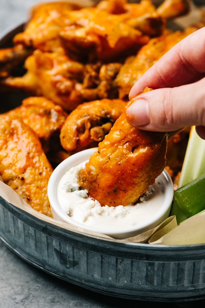 A woman's hand dipping a buffalo wing into a bowl of blue cheese dressing.