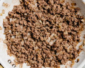 Cooked ground beef with diced onions in a skillet.
