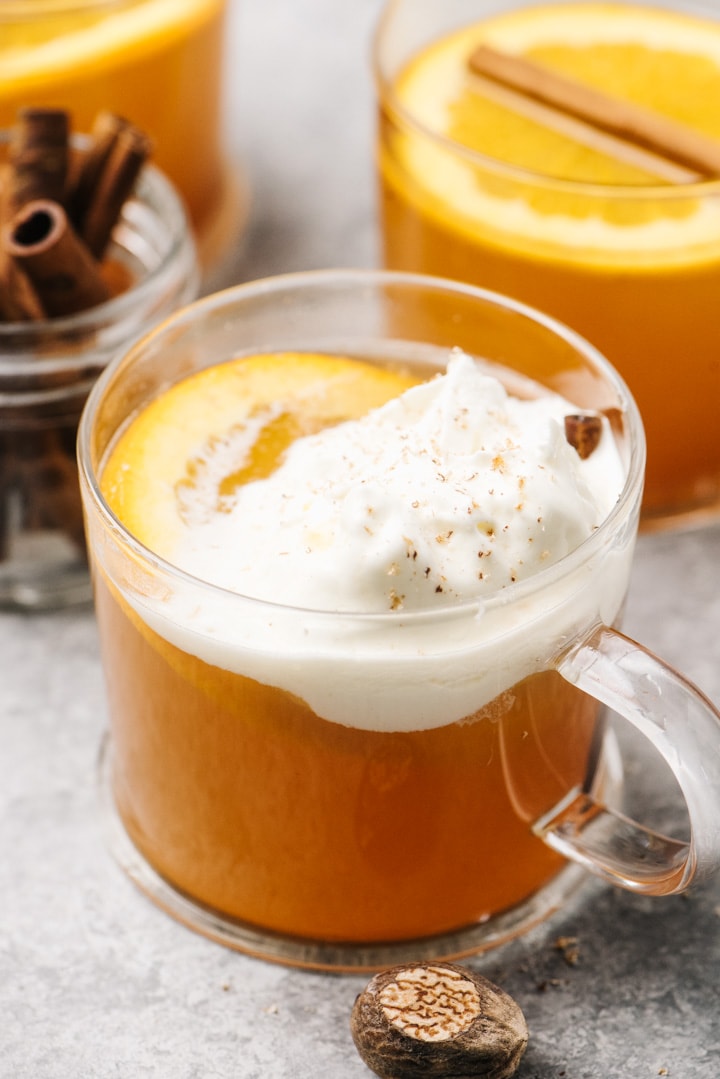 A glass of mulled cider topped with whipped cream and freshly grated nutmeg.