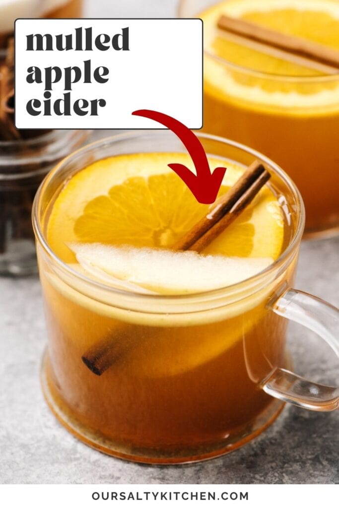 Side view, several mugs of hot apple cider on a concrete background, garnished with orange slices, apple slices, and a cinnamon stick; text overlay reads "mulled apple cider".