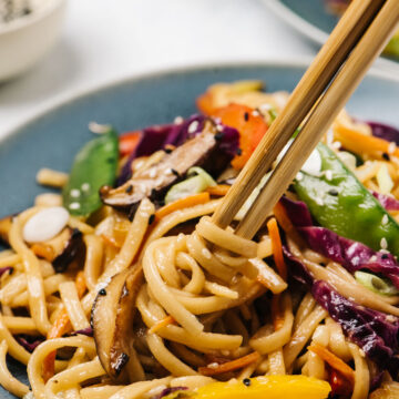 Side view, chopsticks twirling stir fry noodles with rainbow vegetables.