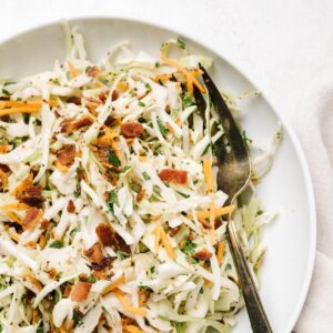 Keto bacon coleslaw in a white bowl with a silver serving fork and white linen napkin.