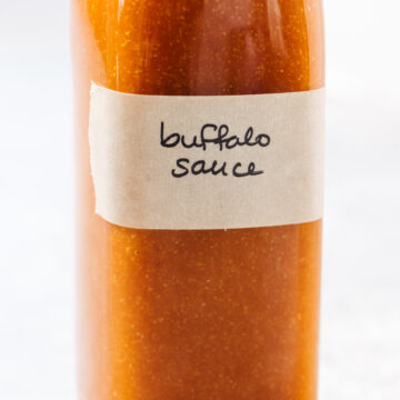 Homemade buffalo sauce in glass bottle with a handwritten label.