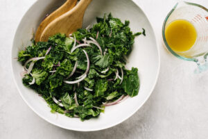 Kale and thinly sliced red onion in a salad bowl tossed with maple vinaigrette.