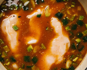 Three whole chicken breasts simmering in taco soup broth.