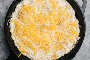 Crab dip in a cast iron skillet sprinkled with cheese before being baked.