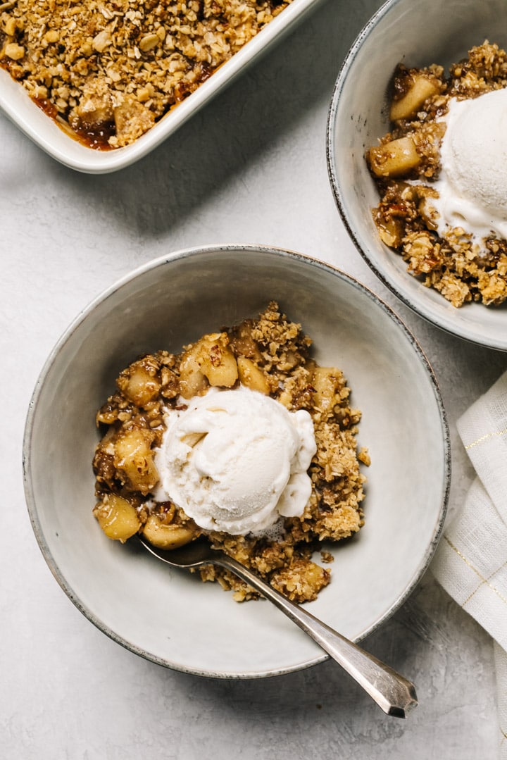 Two bowls of healthy gluten free apple crisp topped with vanilla ice cream on a table with a white linen napkin.