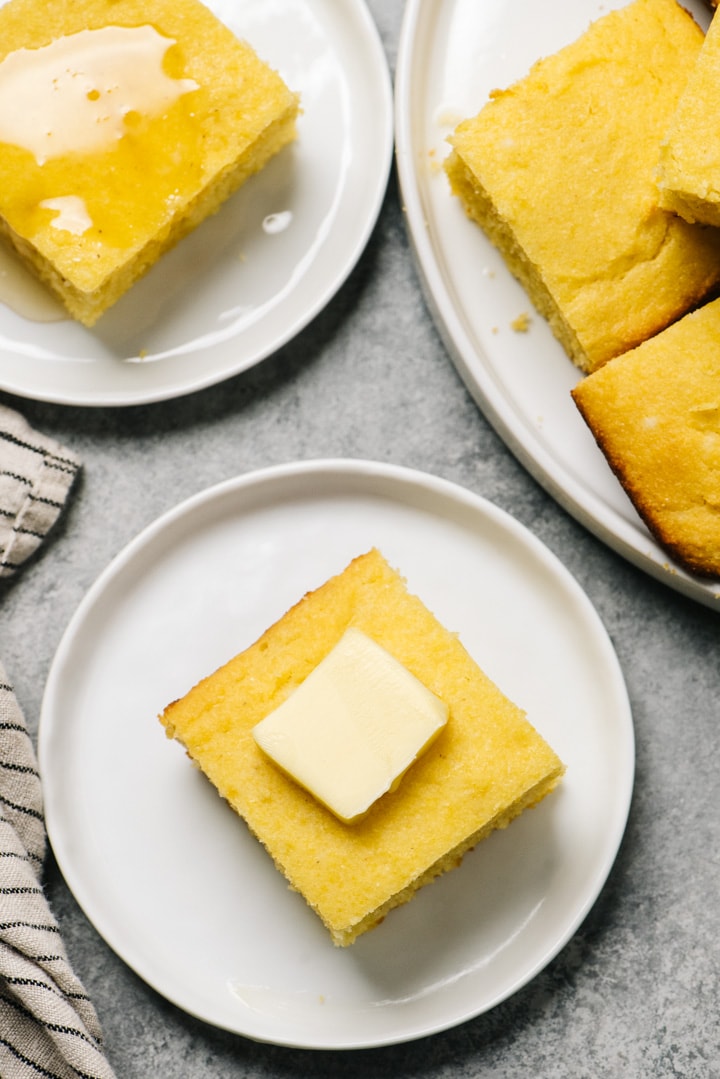 Two pieces of healthy cornbread topped with butter or honey next to a platter.