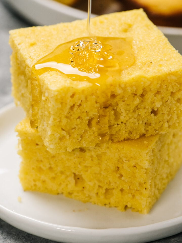 Two pieces of healthy cornbread stacked on a plate, drizzled with honey.